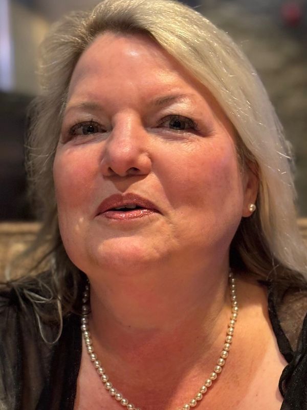 Close-up of a middle-aged woman with blonde hair wearing a pearl necklace and earrings.