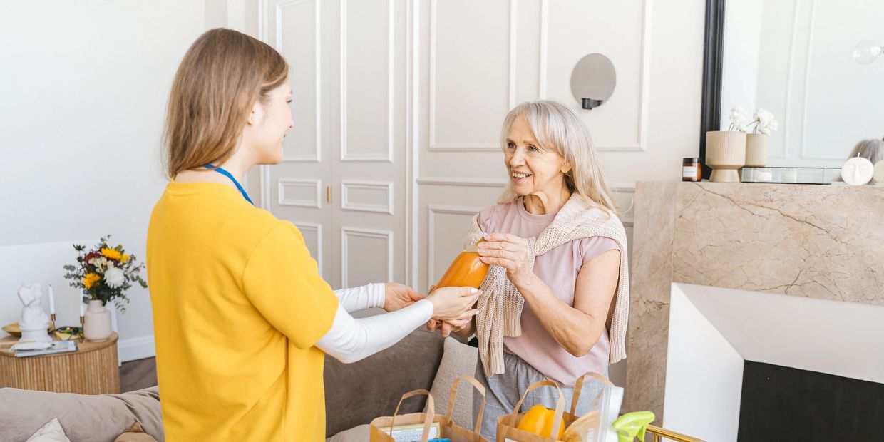 Two women exchanging a bottle in a living room.