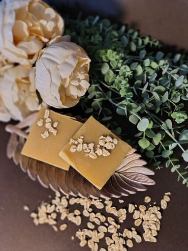 Two oatmeal soap bars on a decorative leaf plate with flowers and green leaves.