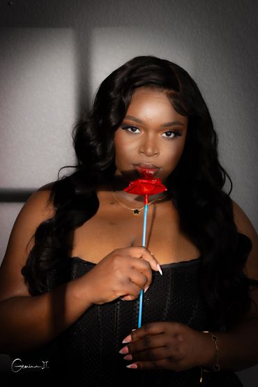 Woman holding a red rose-shaped lollipop close to her lips.
