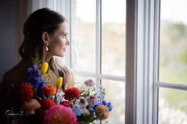 Woman with flowers looking out a window.