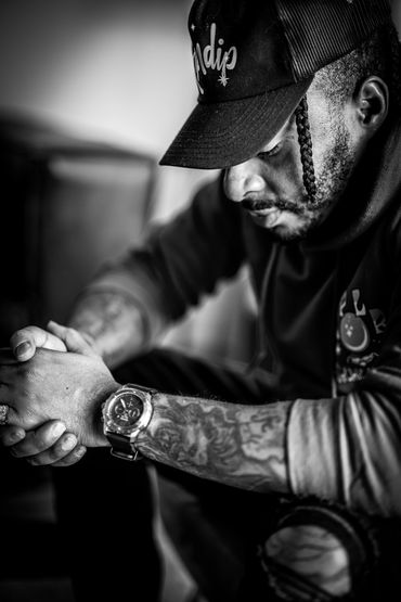 Man in deep thought with hands clasped, wearing a cap and watch.