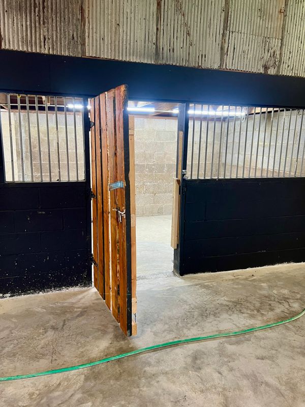 Rustic wooden door partially open in an industrial space with concrete floors and metal bars.