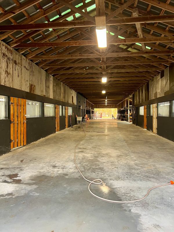 Empty barn aisle with wooden stalls and a hose on the concrete floor.