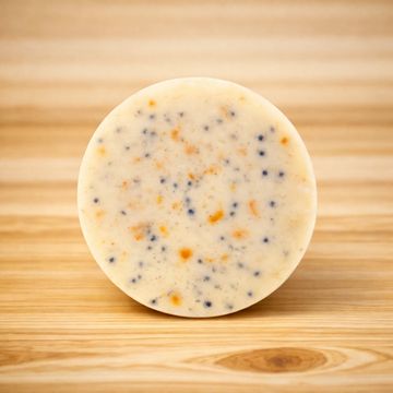 Round soap bar with orange and black specks on wooden surface.
