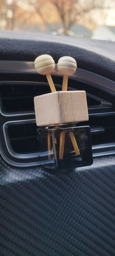 Air freshener attached to a car air vent with wooden and black design.