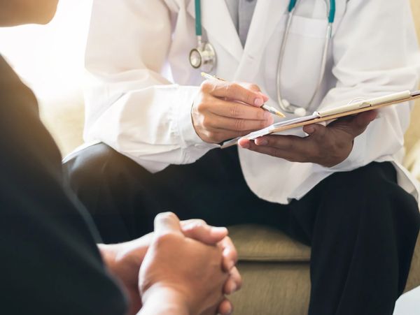 Doctor consulting a patient and taking notes on a clipboard.