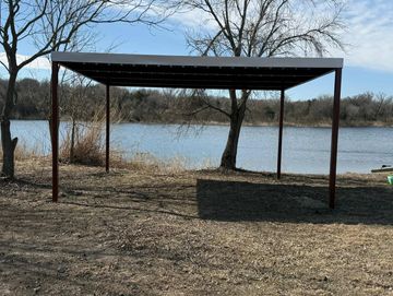 A metal canopy structure by a lakeside on a clear day.
