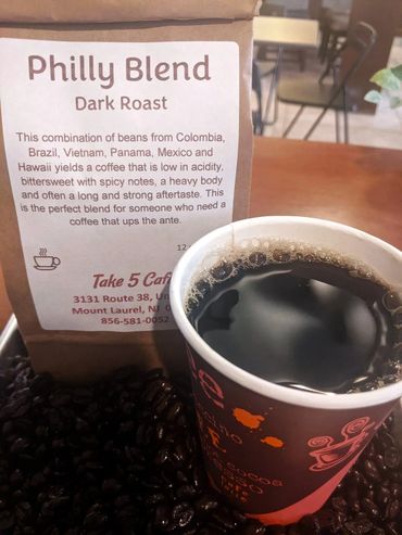 Cup of dark roast Philly Blend coffee next to coffee beans and packaging.