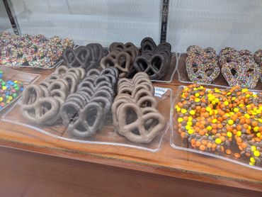 Chocolate-covered pretzels with various toppings displayed in trays.