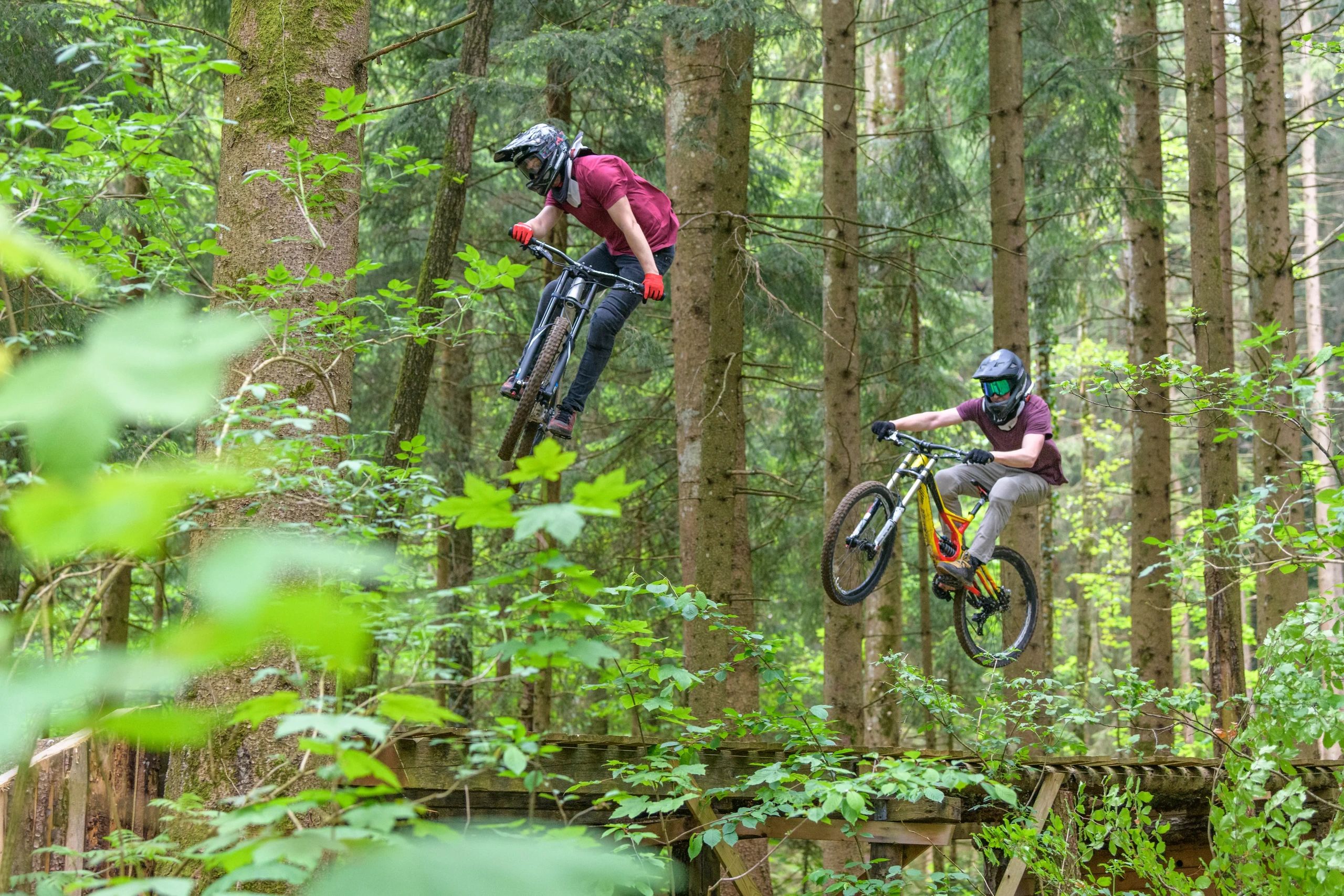 Two cyclists riding technical features in a Pacific northwest forest setting