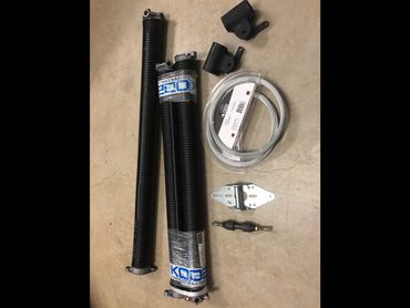 Garage door torsion springs with hardware and cables on a concrete floor.