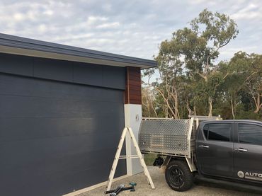 A gray pickup truck parked near a modern garage door with tools and a ladder nearby.