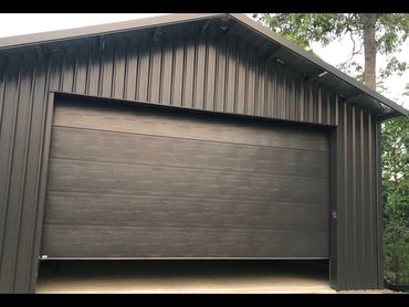 Modern garage door with dark wood texture partially open in a black metal building.