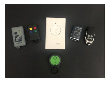 Various garage remote controls and a wall-mounted remote on a black surface.