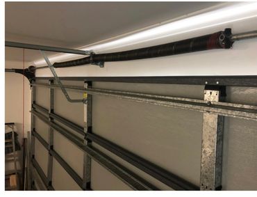 Interior view of a garage door with its torsion spring and metal frame.