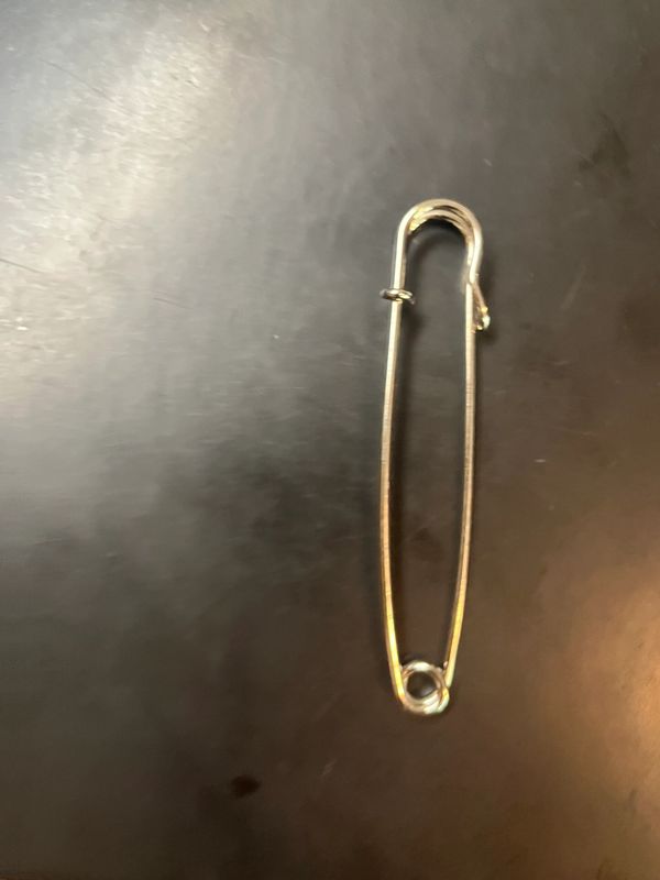 A silver safety pin on a black surface.