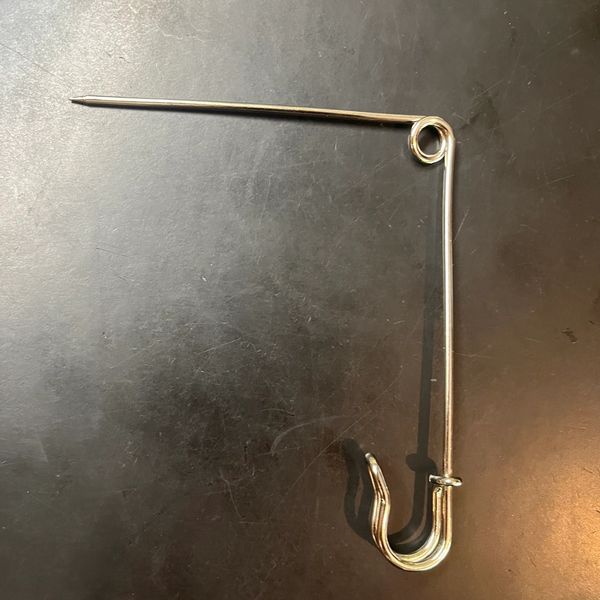 A unique large safety pin with a hook on a dark surface.