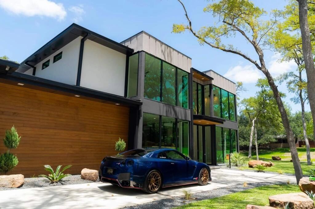 Modern house with glass walls and a blue sports car parked outside.
