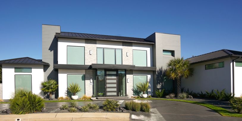 Modern two-story house with large windows and palm trees.