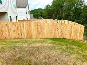 A backyard with a wooden fence and patchy grass.