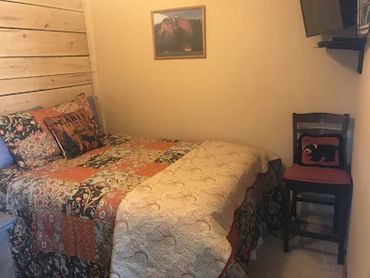 A small bedroom with a bed, a chair, and a painting