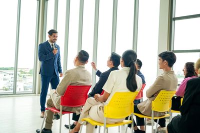 A man in a suit speaking to a seated audience in a bright room.