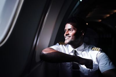 Pilot in uniform smiling by airplane window, bathed in natural light.