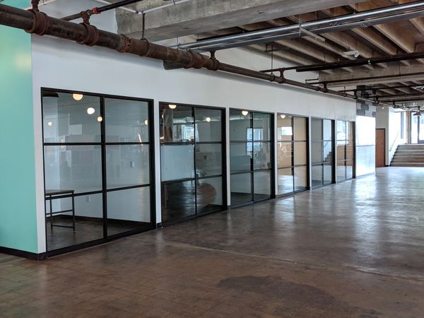 Modern office hallway with glass-walled conference rooms and exposed industrial ceiling.
