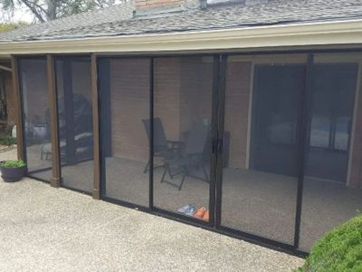 Screened patio with chairs and table behind mesh doors.
