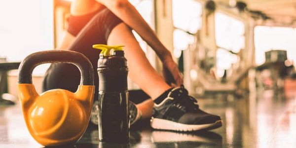 Person stretching in gym with kettlebell and water bottle.