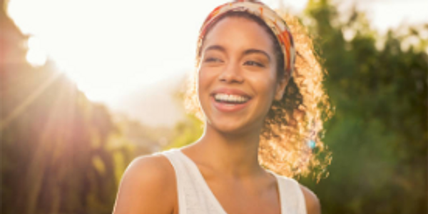 Smiling woman enjoying sunlight outdoors with headband.