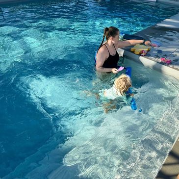A woman and child playing in a pool by the steps with toys.