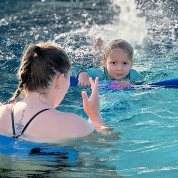 A child and adult enjoying swimming in a pool with a splash background.