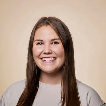 Smiling young woman with long brown hair against a beige background.