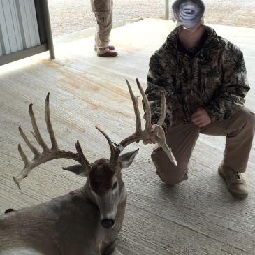 Man posing with a large buck deer indoors.