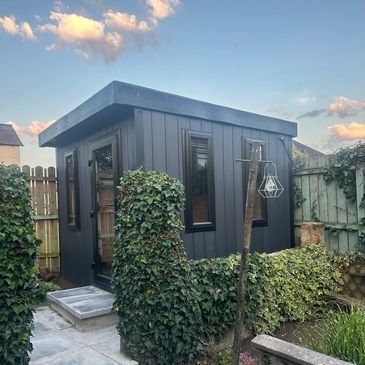 Modern black garden shed with ivy in a fenced backyard.