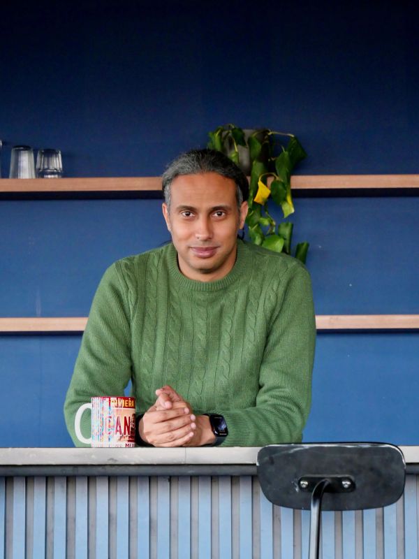 Man in green sweater sitting at a counter with a colorful mug.