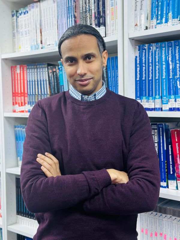 Man in maroon sweater standing in front of bookshelves.