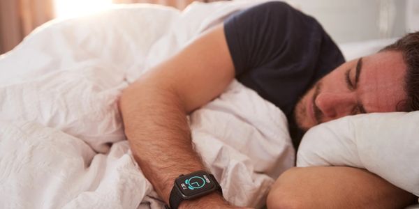 Man Asleep In Bed Wearing Smart Watch As Sun Breaks Through Curtains