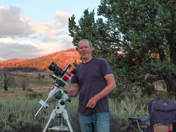 A medium shot shows a man standing next to a camera mounted on a tripod.