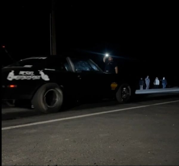 Black car on road at night with person holding light.