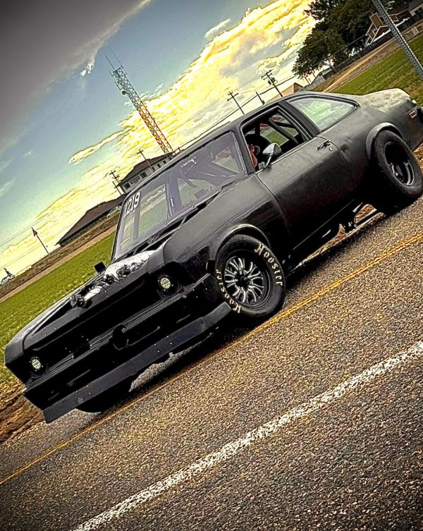 Matte black race car on a road at sunset.