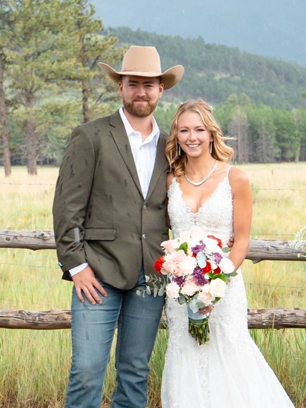 Bride and groom standing outdoors by a rustic fence.