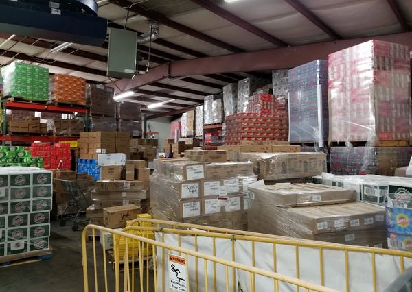 Warehouse filled with stacked pallets of boxed goods and a yellow safety barrier.