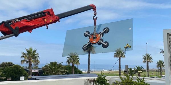 Crane lifting a large glass panel with suction cups on a coastal property.