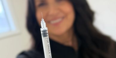 Close-up of a syringe held by a smiling woman in the background.