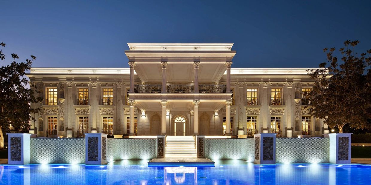 Luxurious illuminated mansion with a grand pool at night.