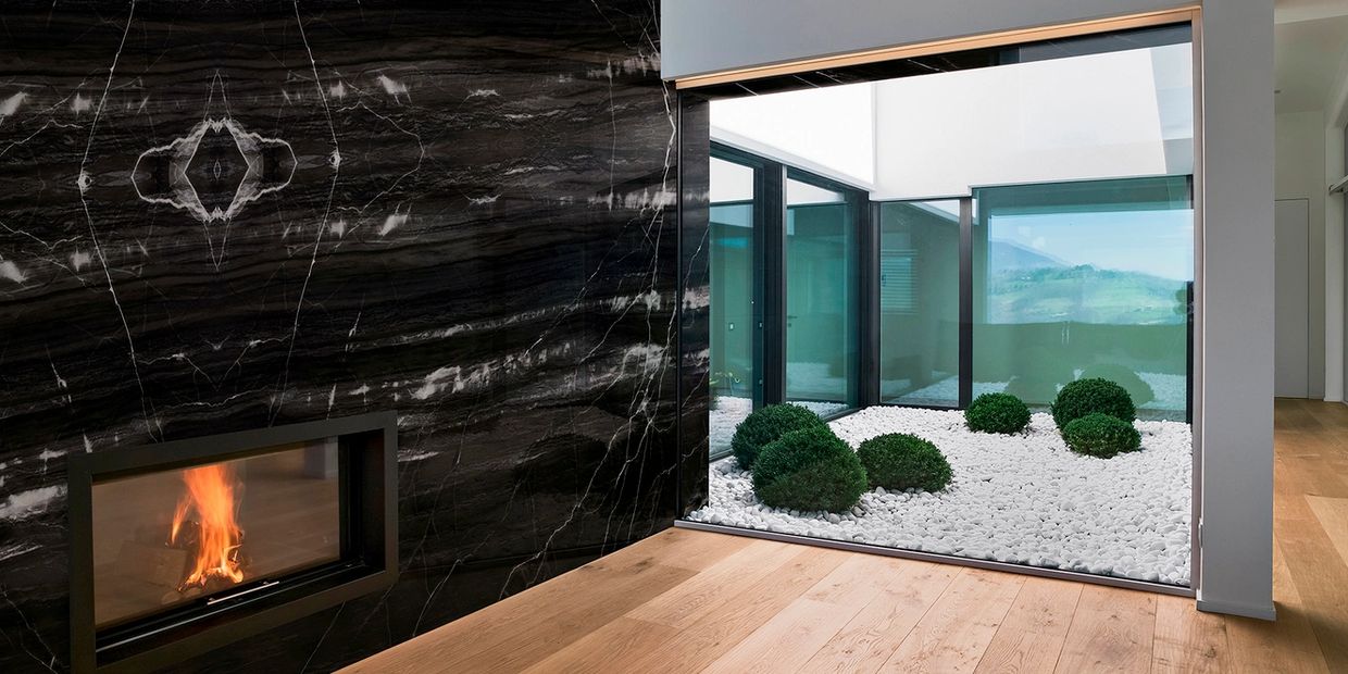 Modern interior with a black marble fireplace and a courtyard garden with white stones and green shrubs.