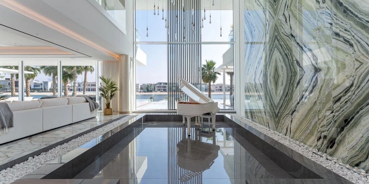 Luxurious modern living room with a white grand piano and large windows overlooking water and palm trees.
